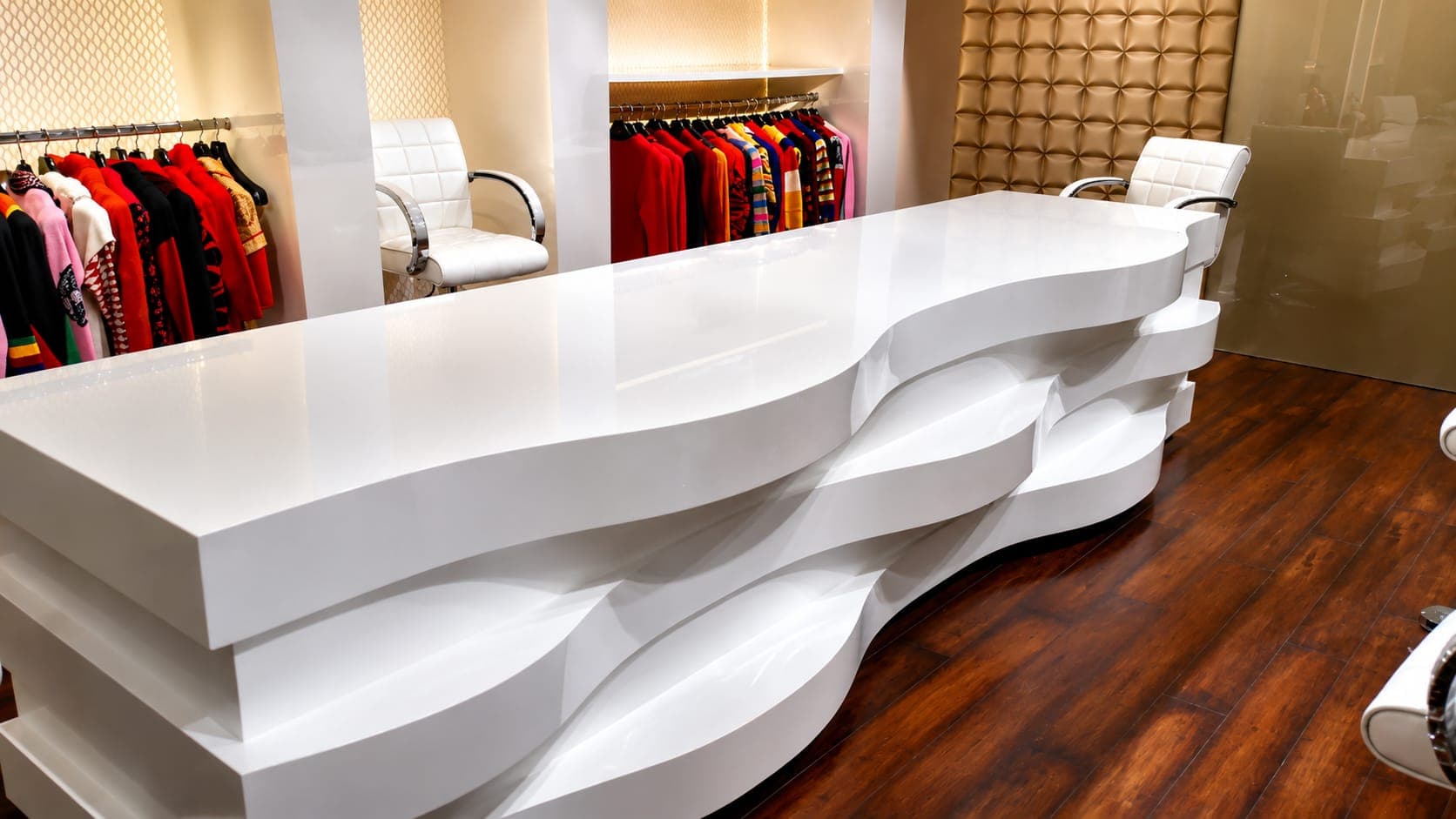 Custom white wave reception counter in the hosiery sample room, Ludhiana, with white-lacquer display alcoves and hosiery collections behind