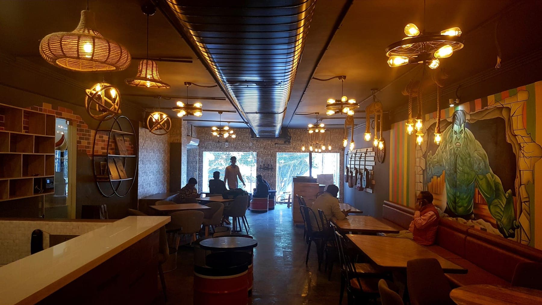 Dining hall with exposed duct, rope pendants, wagon-wheel fixtures and booth seating, FiTreat restaurant, Ludhiana
