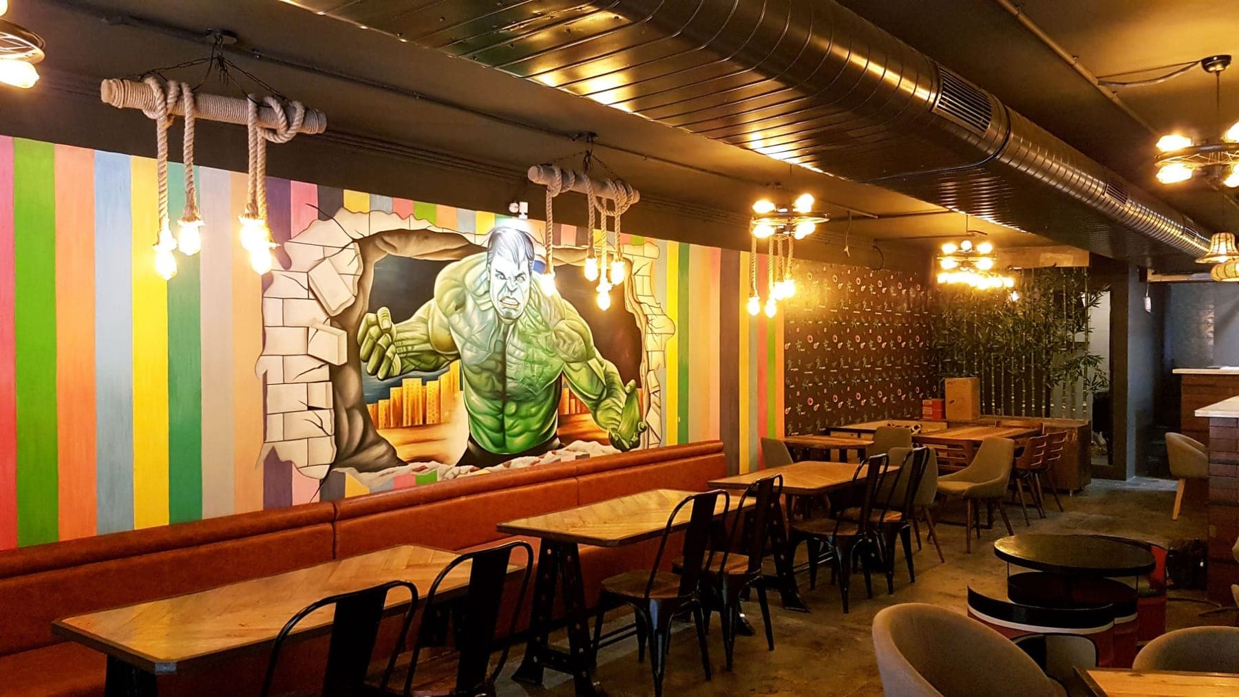 Multicolour vertical stripe wall with the Hulk mural and rope pendant lights above booth seating, FiTreat restaurant, Ludhiana