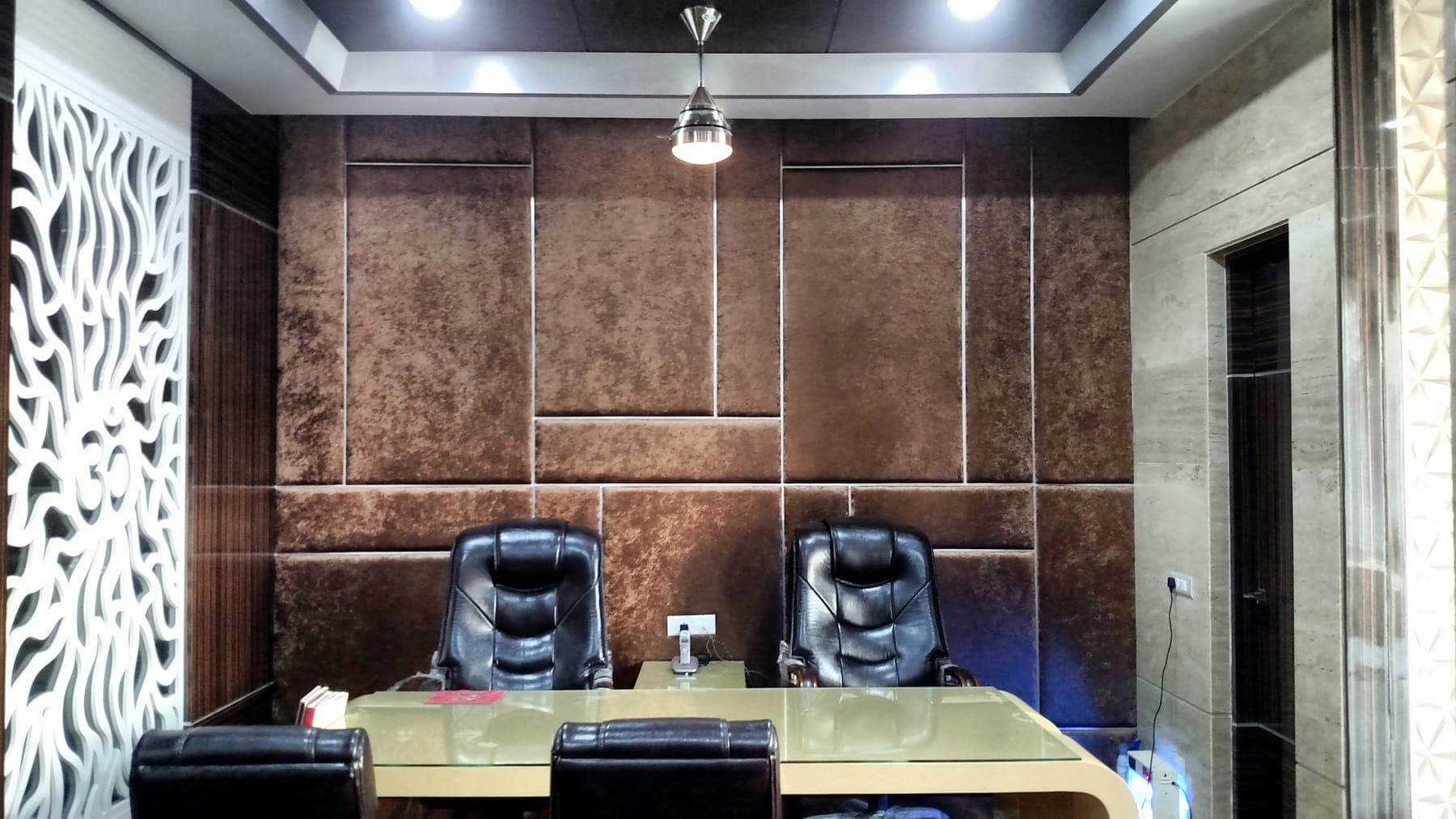 Executive office with a tufted leather feature wall in chocolate and tan, leather chairs and a glass-top desk, Ludhiana
