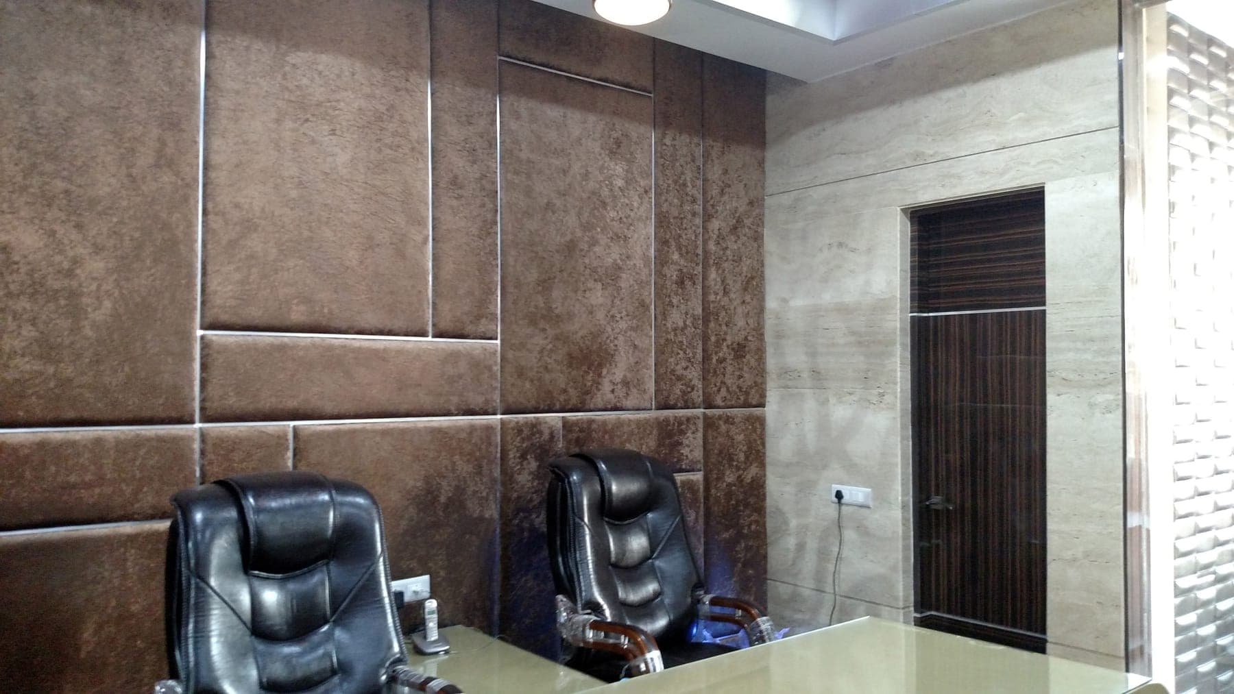 Quilted leather wall panels beside a travertine-look wall and wood door in the executive office, Ludhiana
