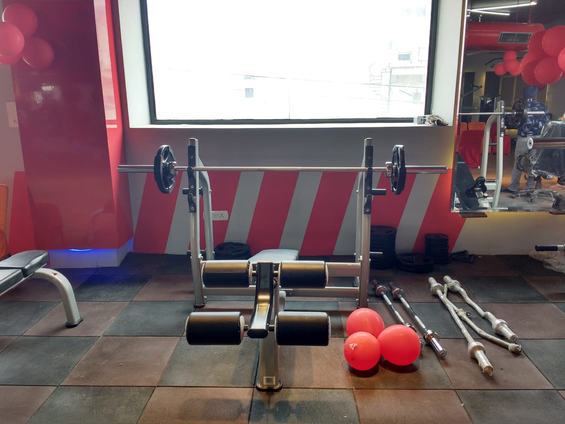 Free-weights zone with a red and grey diagonal-striped wall and rubber flooring, Quillian Gymnasium, Ludhiana