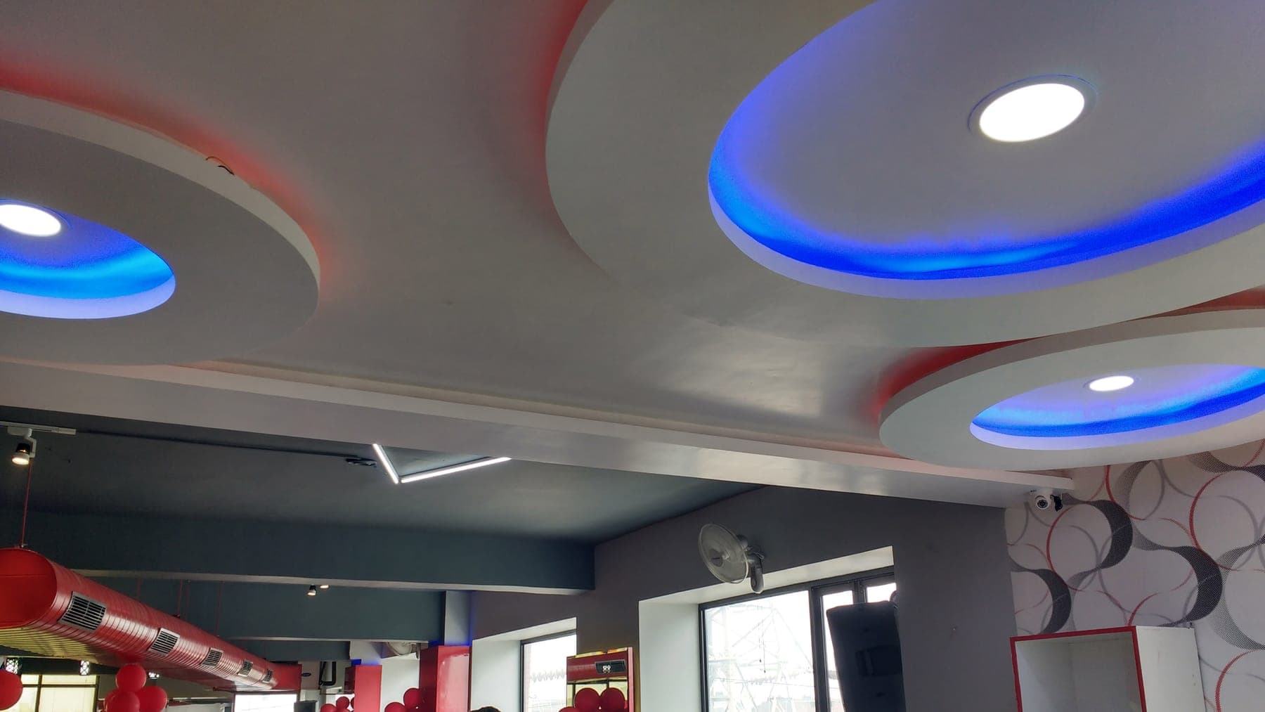 Quillian Gymnasium interior in Ludhiana — circular halo false ceilings with blue LED cove lighting and red accents