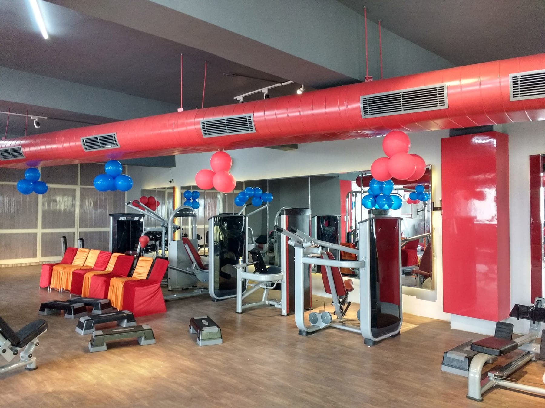 Exposed red air ducting over the workout floor at Quillian Gymnasium, Ludhiana, with mirrored walls and gloss red columns