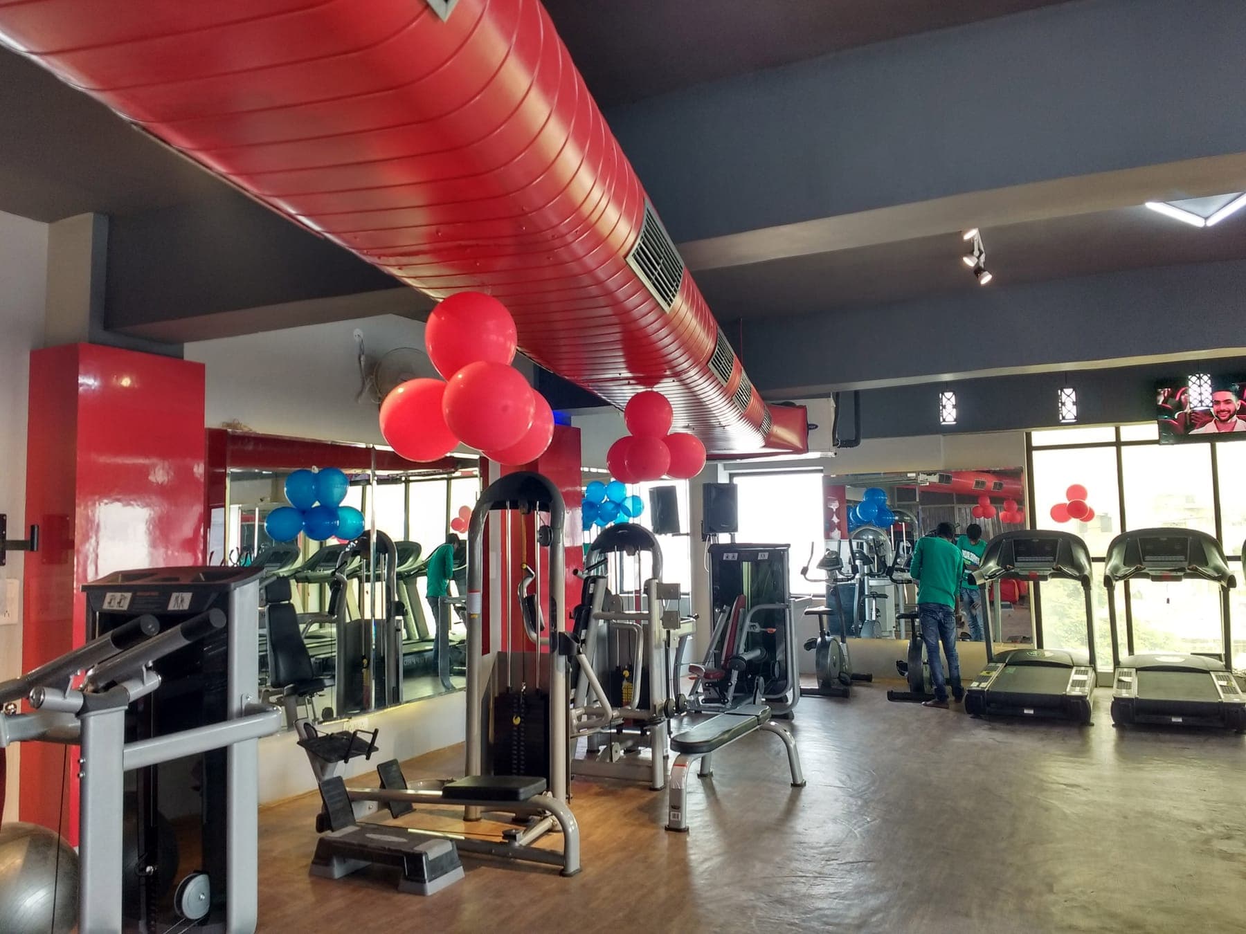 Strength machines beneath the red air duct beside high-gloss red columns, Quillian Gymnasium, Ludhiana