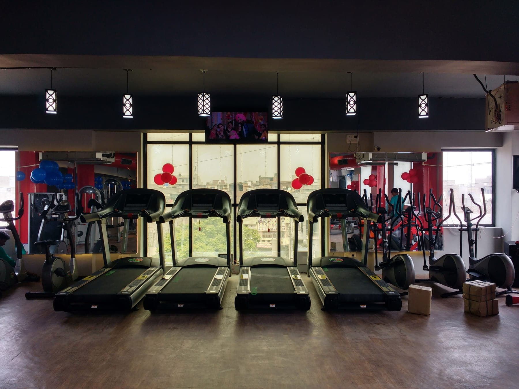 Row of treadmills facing a full-height window, with pendant lights, at Quillian Gymnasium, Ludhiana