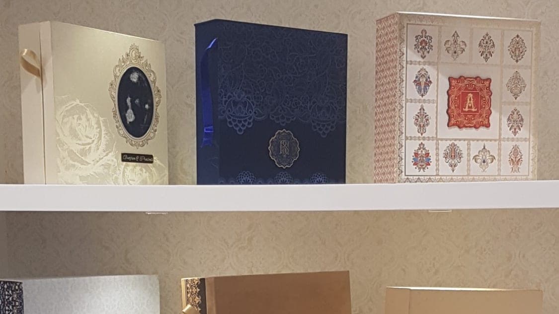 Wedding invitation boxes displayed on white shelves with warm LED spotlights and textured wallpaper, Sentiments Card Gallery, Khanna